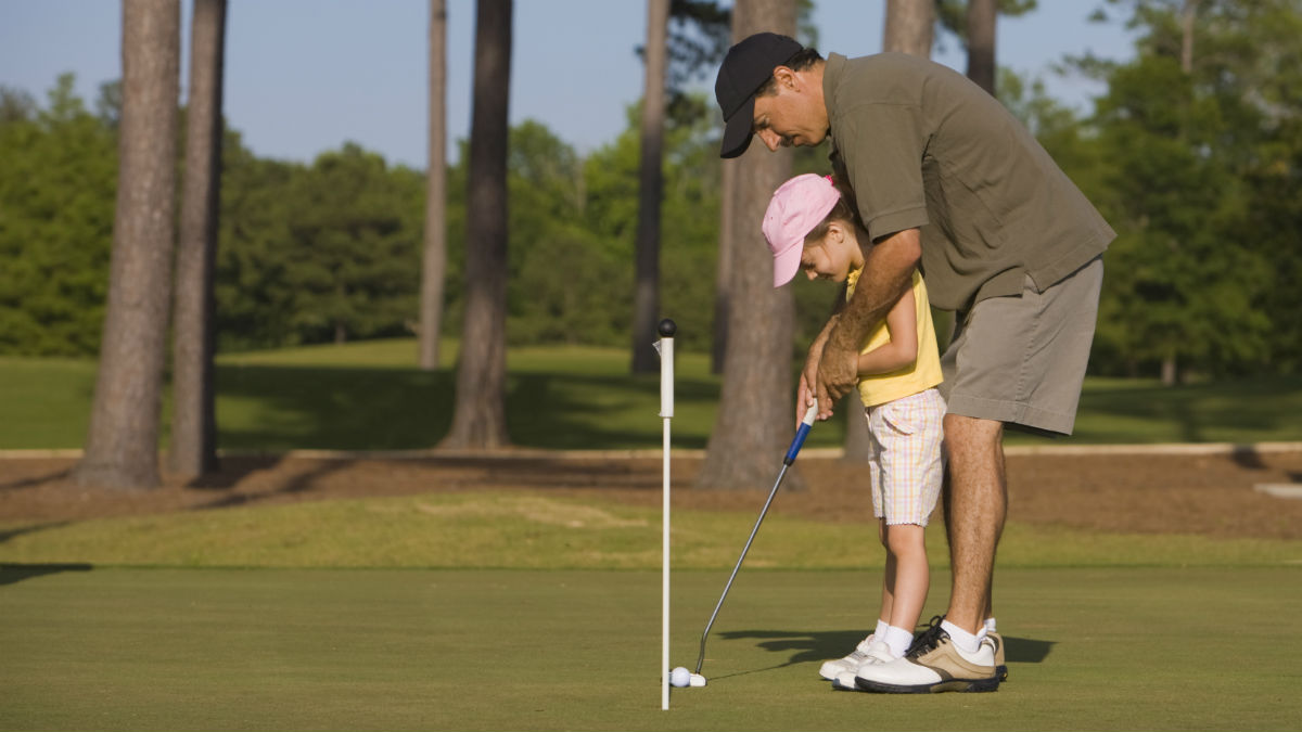 Father teaching daughter how to play golf on father's day