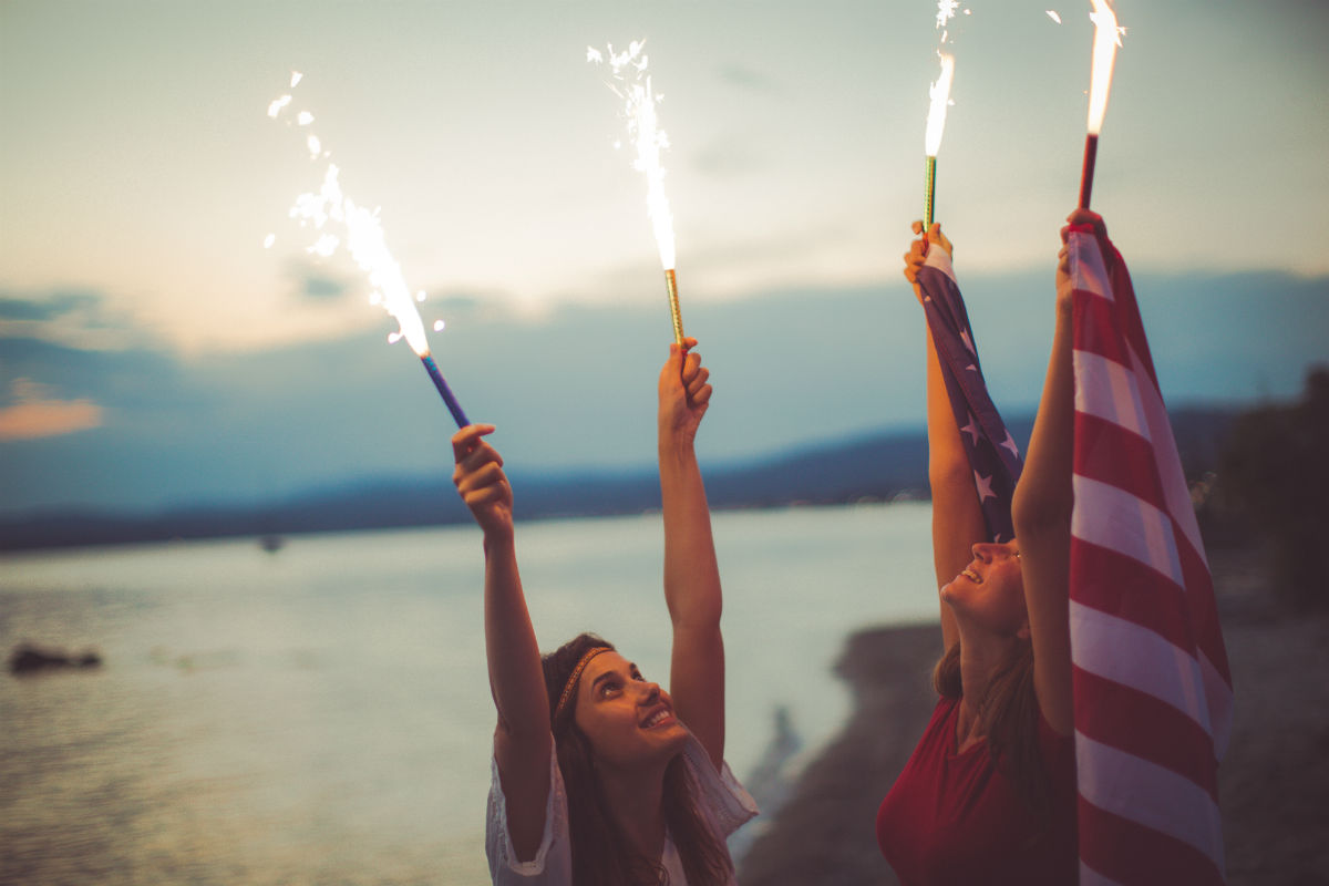 Young girls at the beach, celebrating the fourth of July - by holding an American flag and fire torches up high